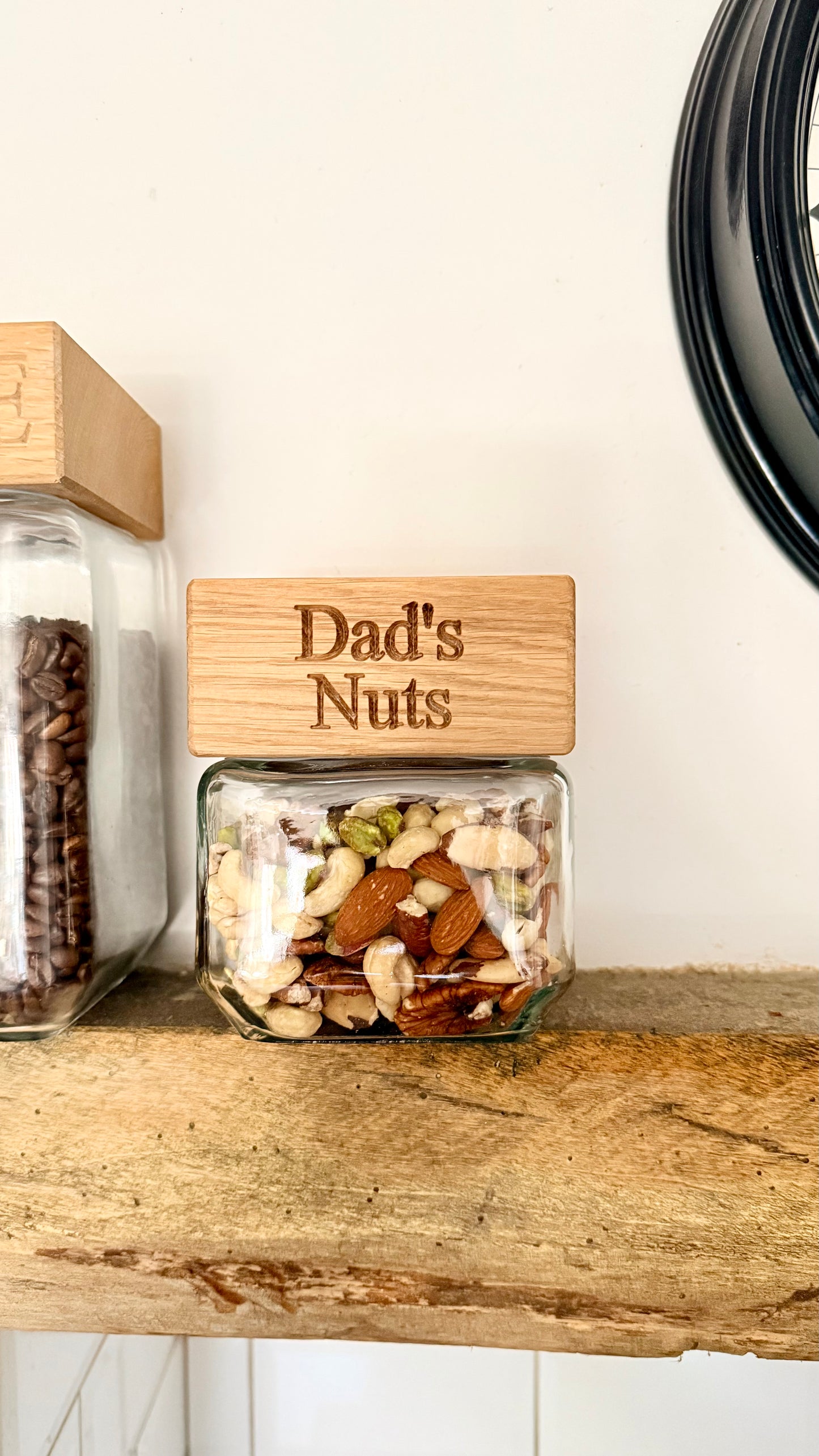Jar labeled 'Dad's Nuts' on a wooden shelf with another jar in the background.