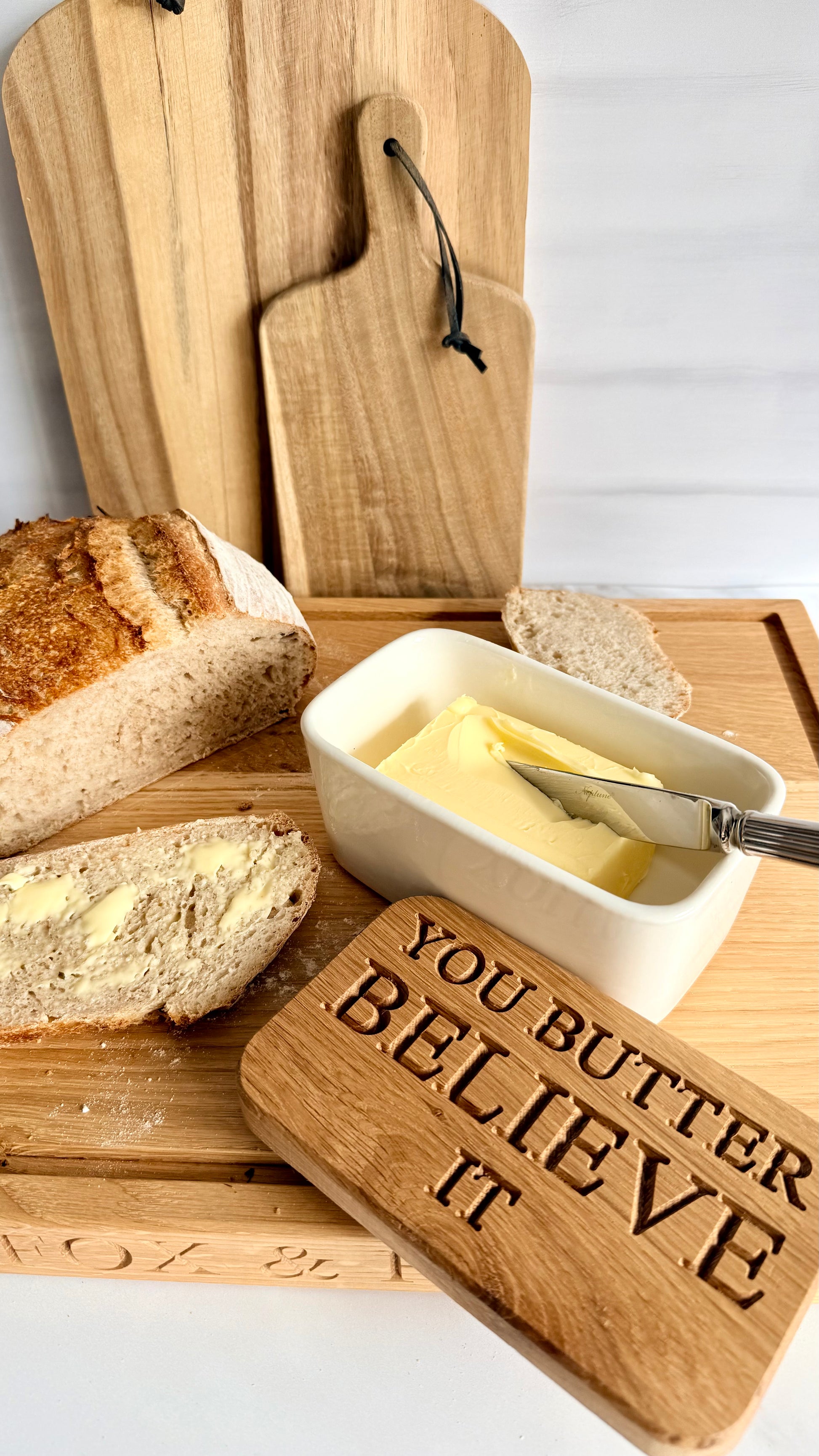 Butter dish with bread and a wooden sign saying 'You Butter Believe It' on a wooden cutting board.