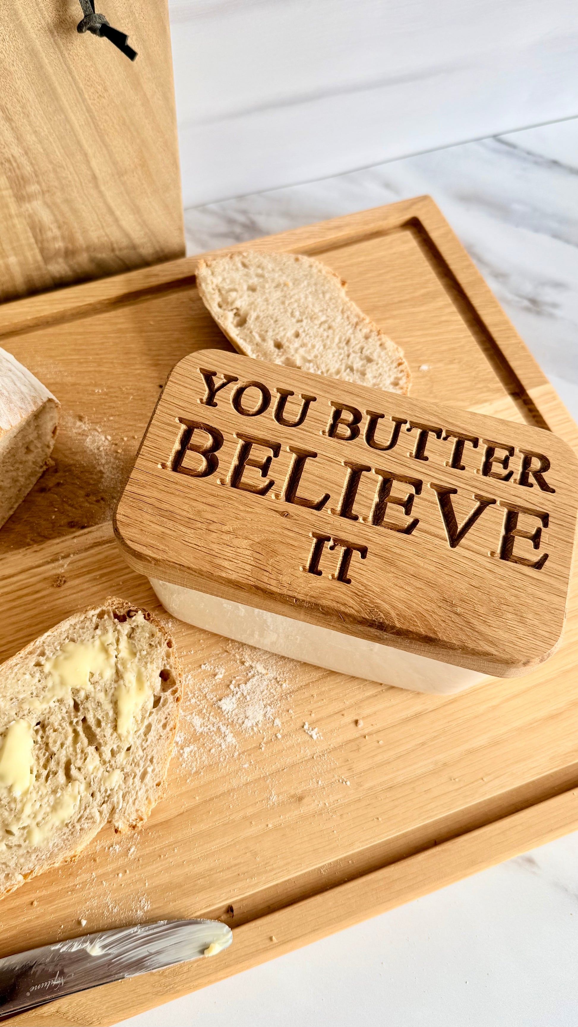 Wooden butter dish with 'You Butter Believe It' text on a marble surface.