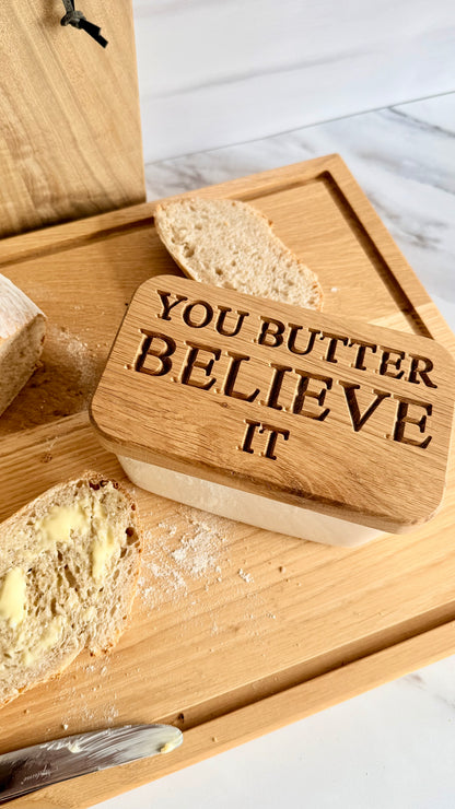 Wooden butter dish with 'You Butter Believe It' text on a marble surface.