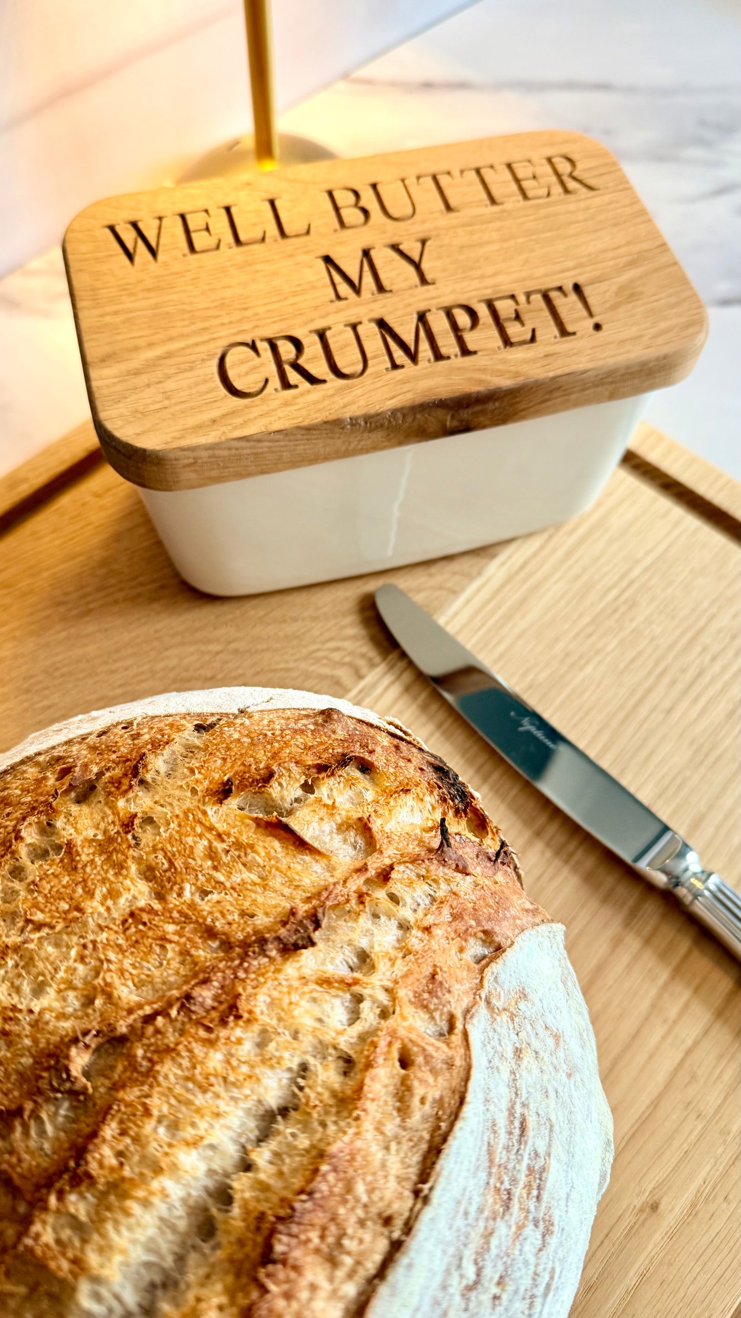 Butter dish with 'Well Butter My Crumpet!' lid on a wooden board with bread and knife.