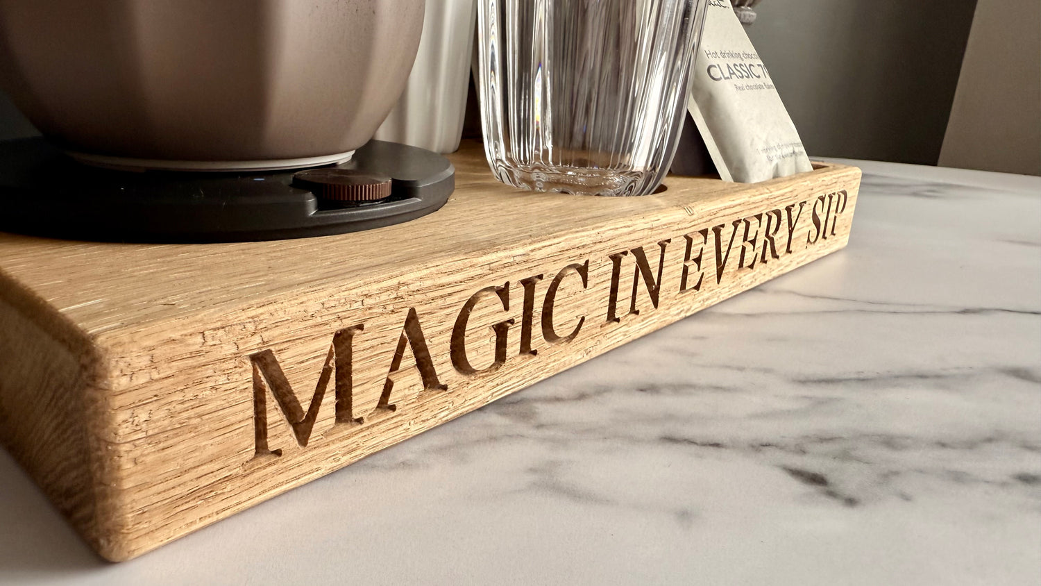 Wooden tray with 'Magic in Every Cup' engraving on a marble surface.