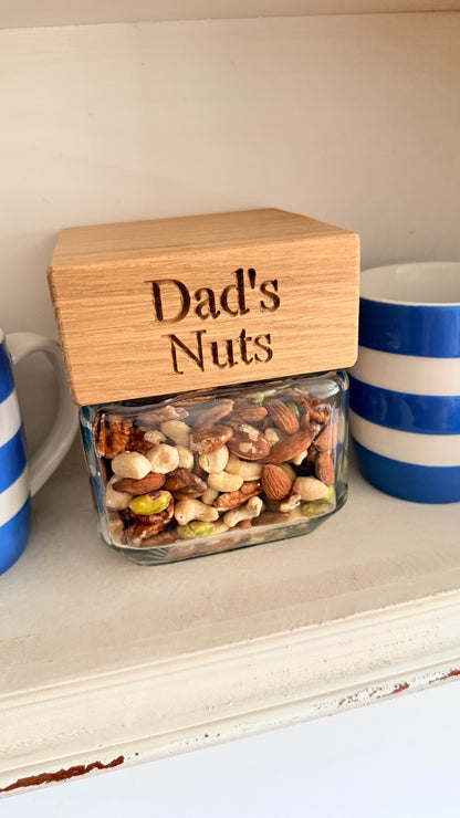 Glass jar with wooden lid labeled 'Dad's Nuts' on a shelf.