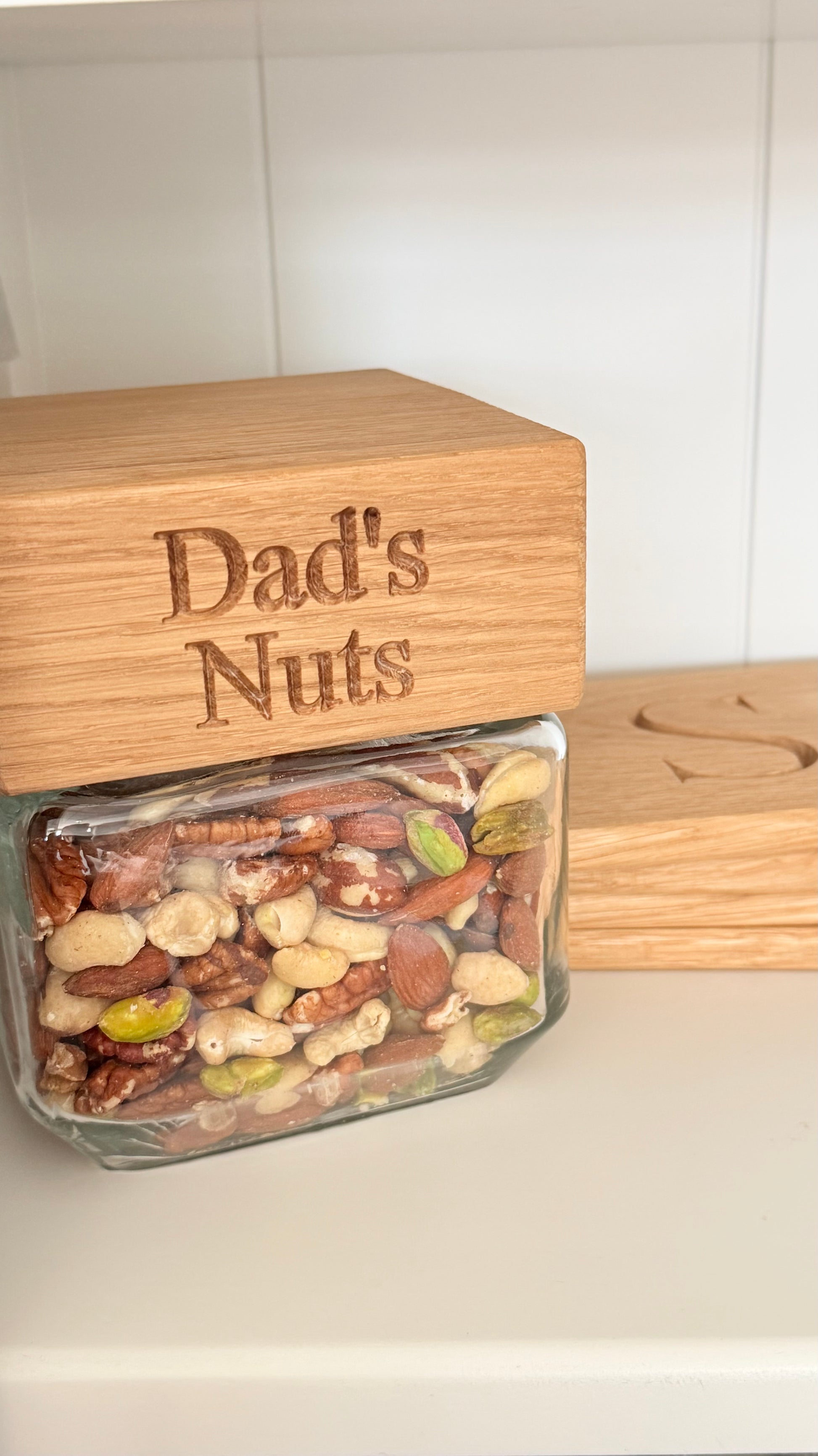Glass jar filled with mixed nuts labeled 'Dad's Nuts' on a wooden lid.
