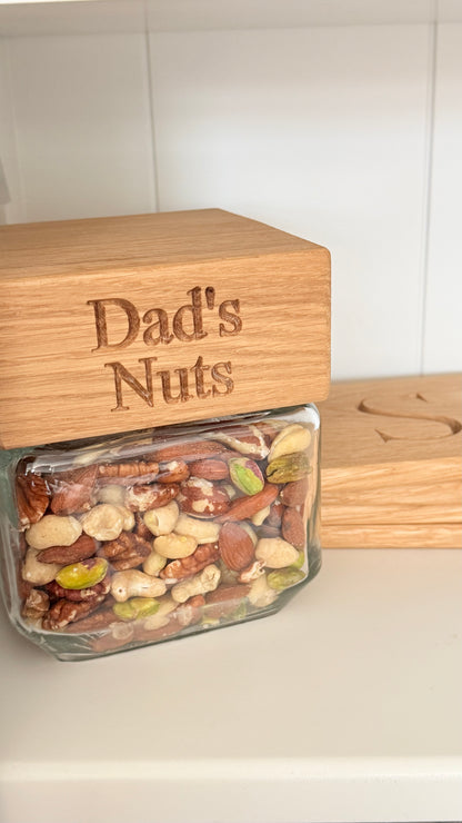 Glass jar filled with mixed nuts labeled 'Dad's Nuts' on a wooden lid.