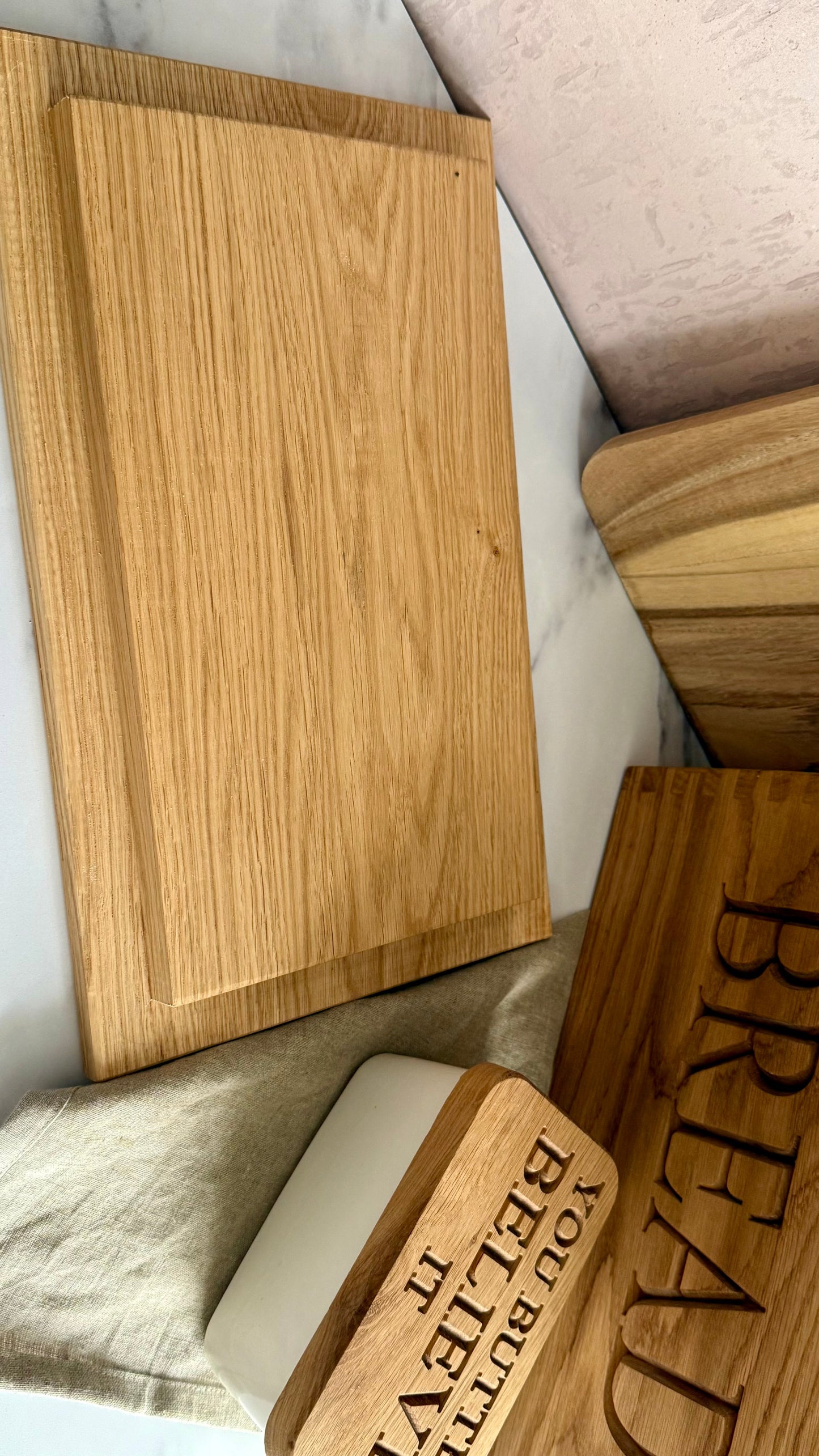 A set of wooden kitchen accessories including a large rectangular cutting board, a smaller wooden bread board engraved with 'BREAD', a wooden butter dish with 'YOU BUTTED IT BELIEVE IT', and a white butter container, all arranged on a marble surface.